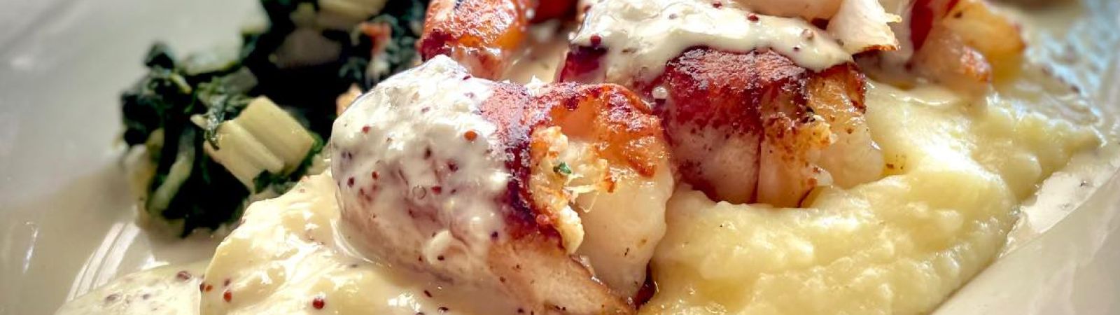 bacon-wrapped prawns stuffed with crab served on polenta with sauteed greens